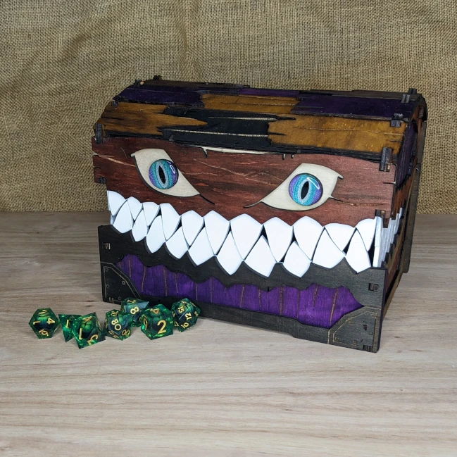 Large handcrafted wooden mimic chest with purple finish and green and purple eyes, displayed with tabletop gaming dice.